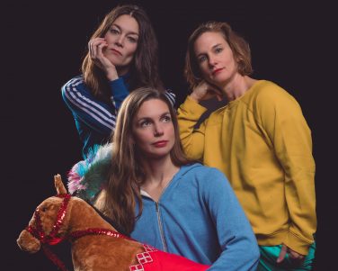 Three circus performers and one is holding a toy pony.