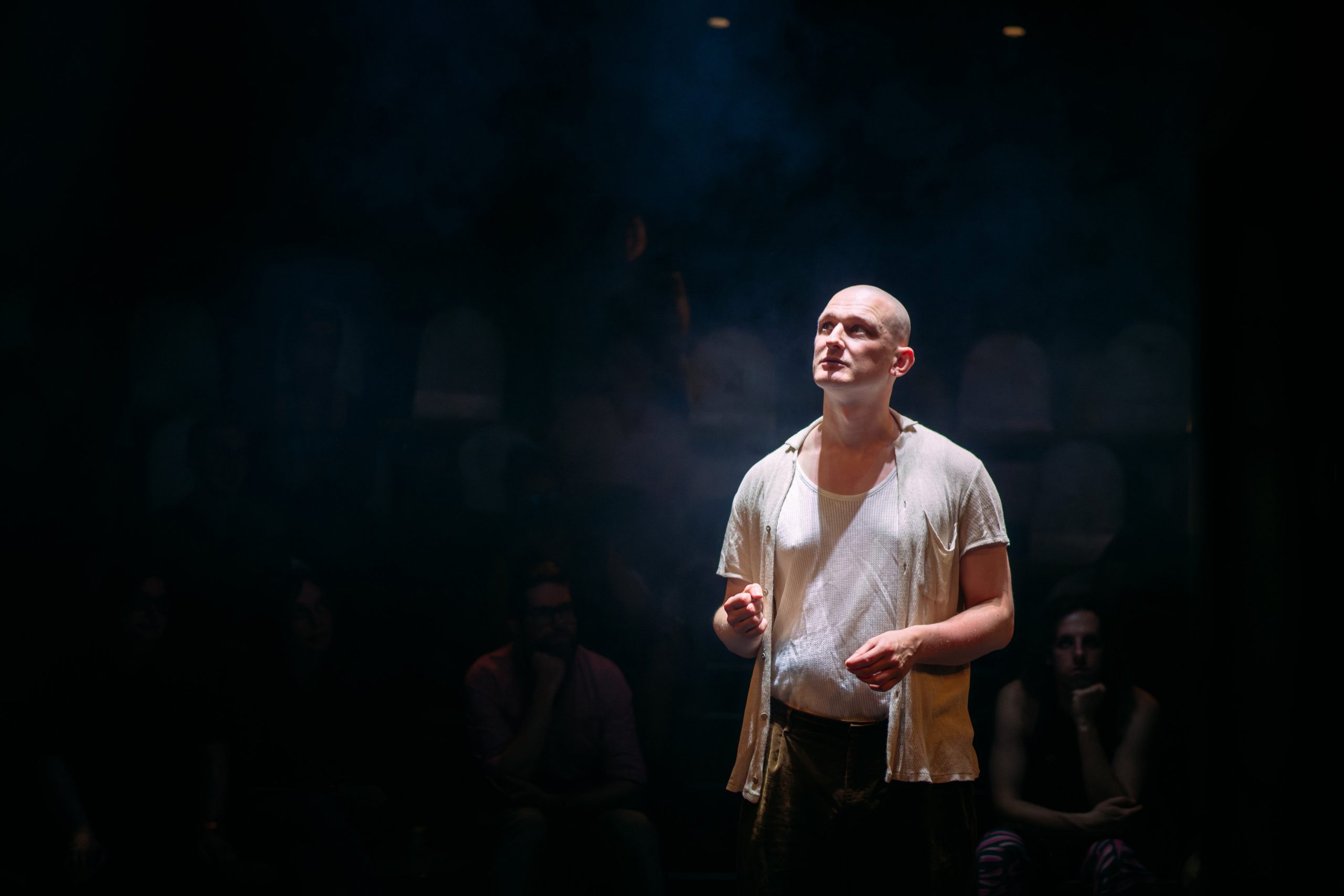 Sam Ward is performing in almost darkness, wearing a white shirt.