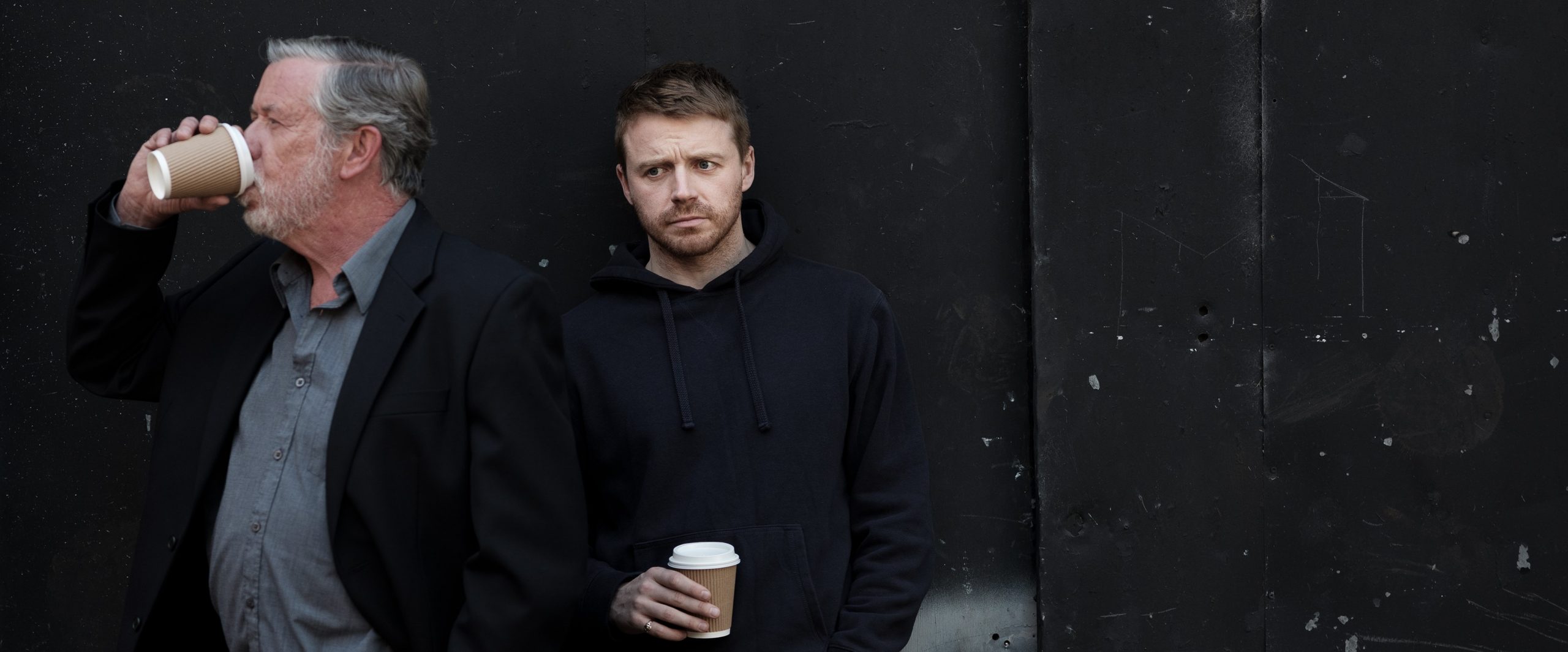 Two men holding coffee cups against a dark background.