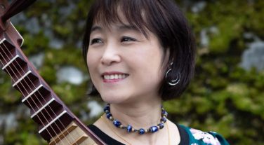 Wu Man is smiling with a verdant background.