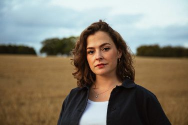 Head and shoulders portrait of musician Katherine Priddy standing in a field.