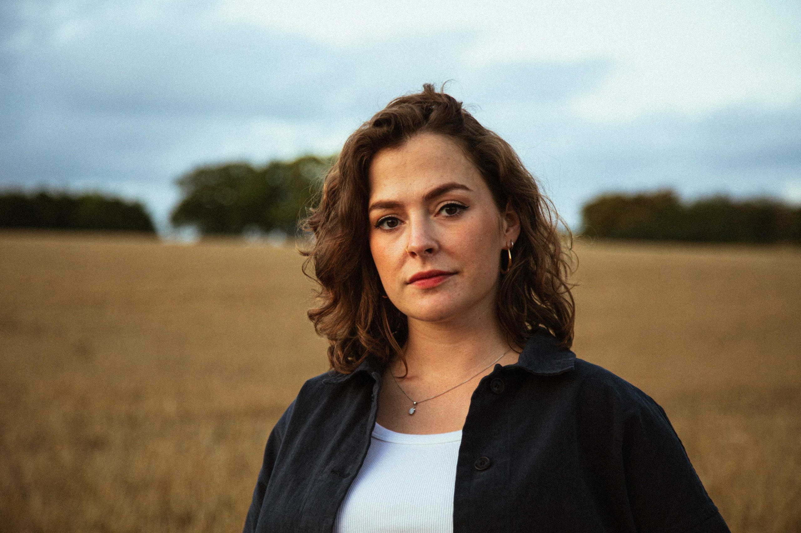 Head and shoulders portrait of musician Katherine Priddy standing in a field.