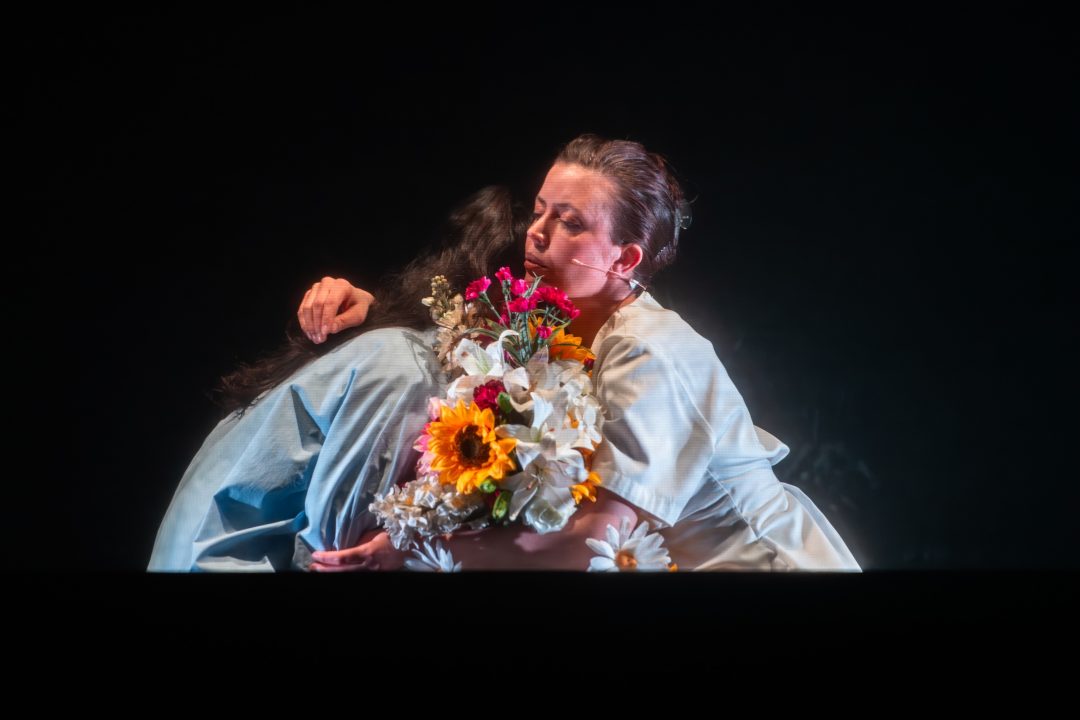 Lærke Schreve Engelbrecht and another actor crouching in an embrace, holding a bouquet of flowers.