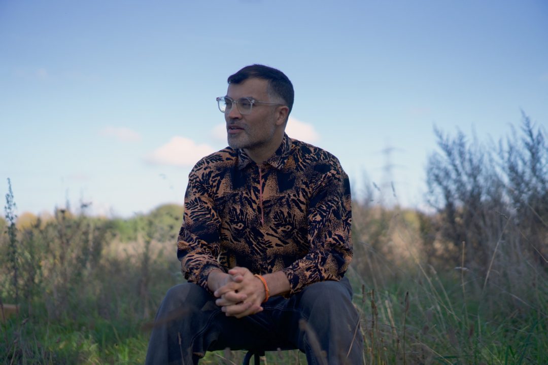 photo of Brian d'Souza sat on a stool, in an overground field.