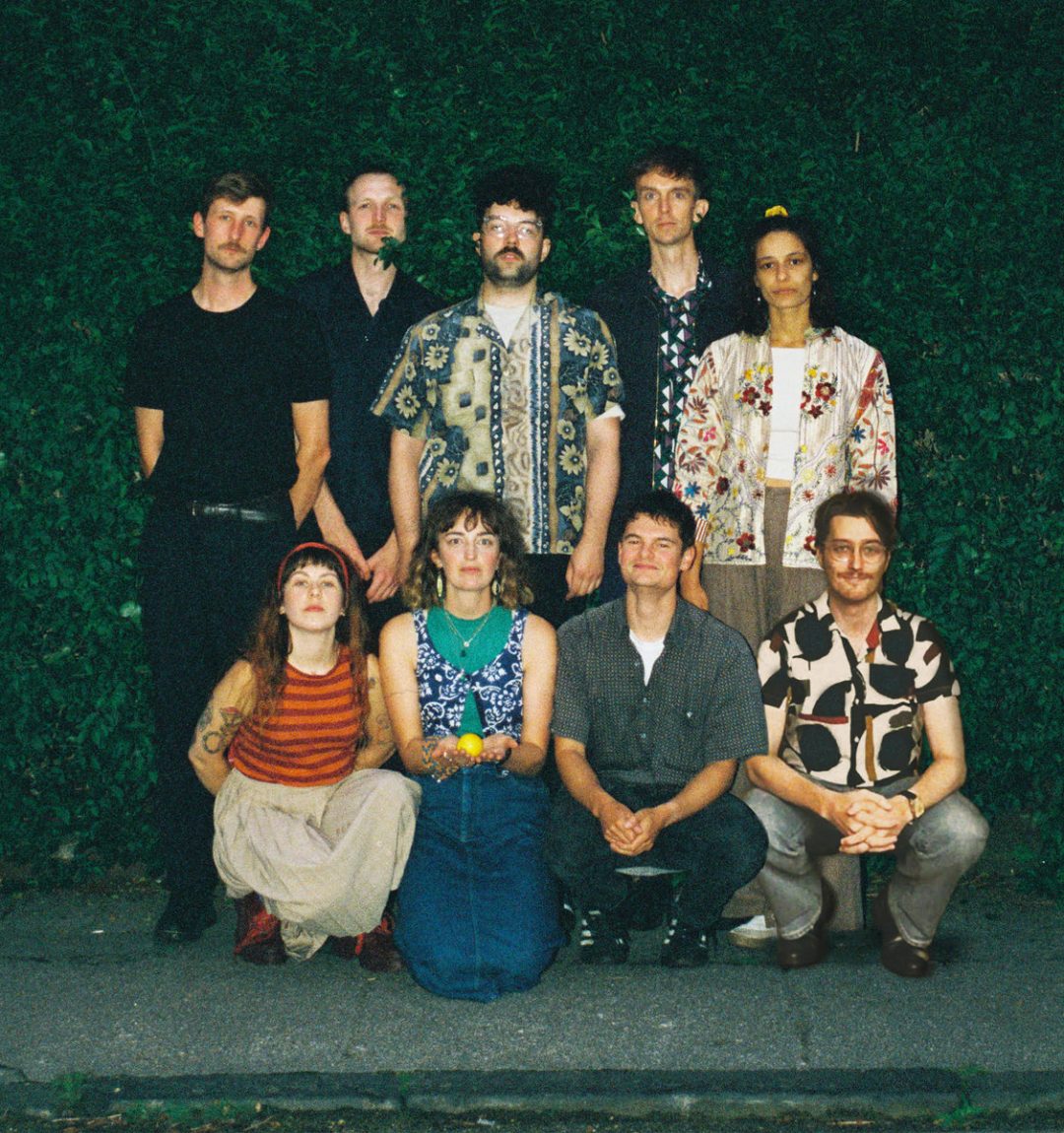 Group of alternative music artists posing outdoors against a green foliage backdrop