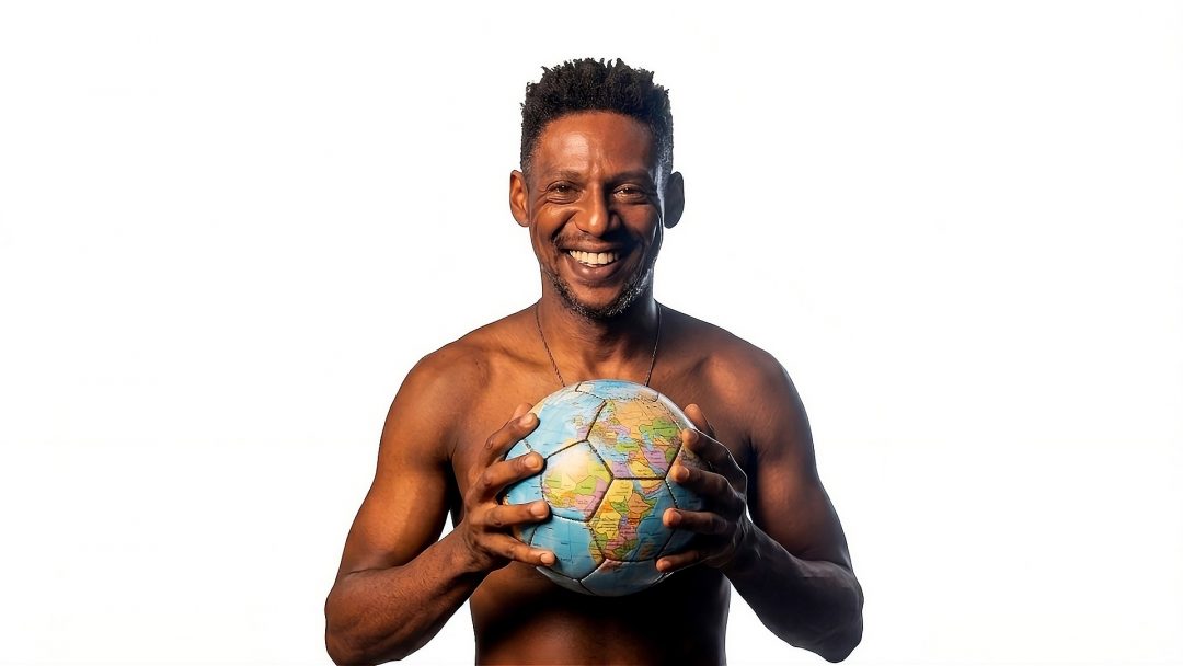 A smiling shirtless performer holding a football styled like a globe against a white background for the Edinburgh Fringe theatre production Dribble.