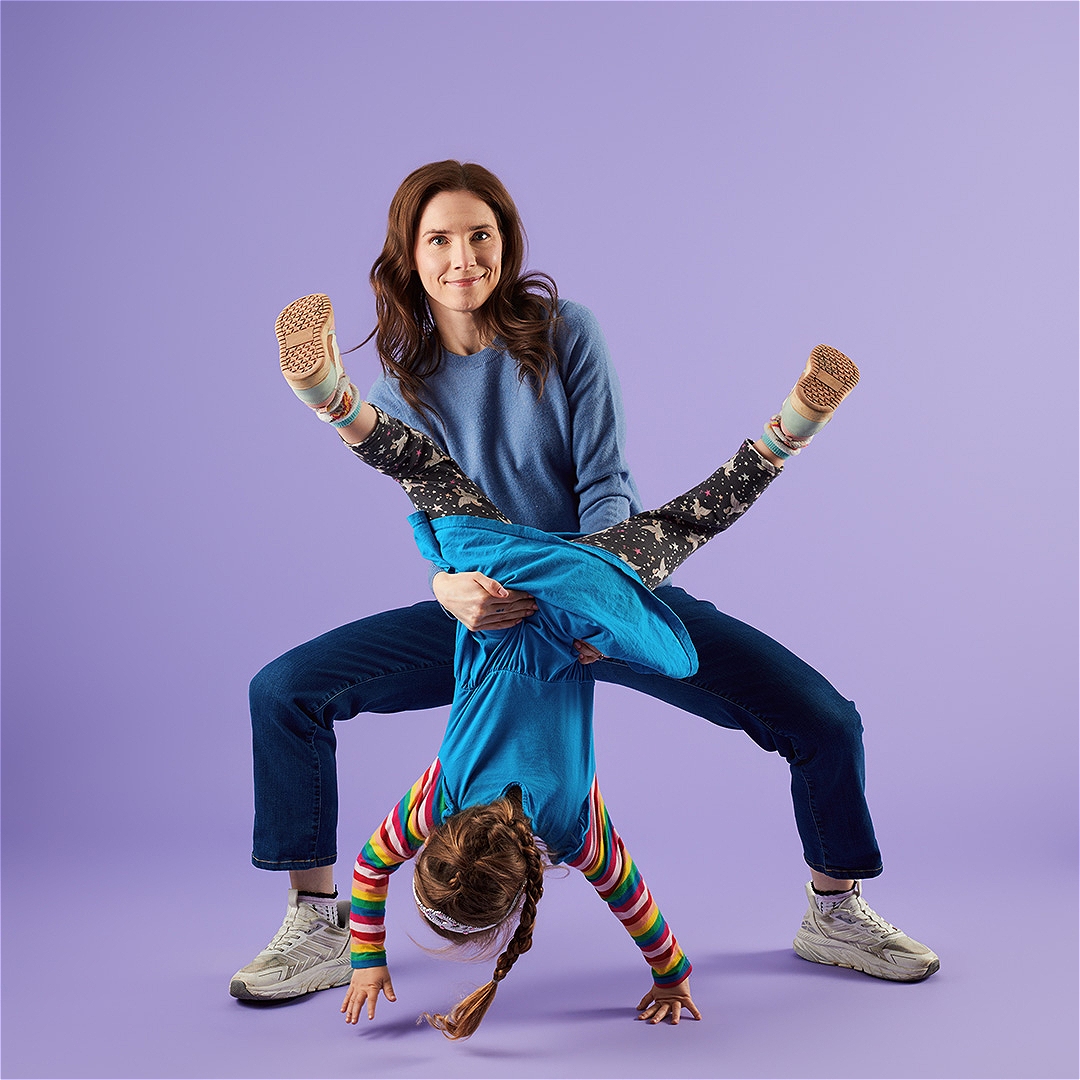 Amanda Knox holding her young daughter upside down in fro=nt of a purple backdrop.