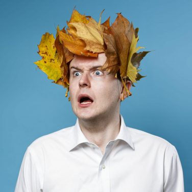Andrew Doherty wearing a crown of autumn leaves against a blue background with a wide-eyed, shocked expression.