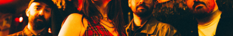 Bikini Body band members posing together under warm red lighting outdoors at night.