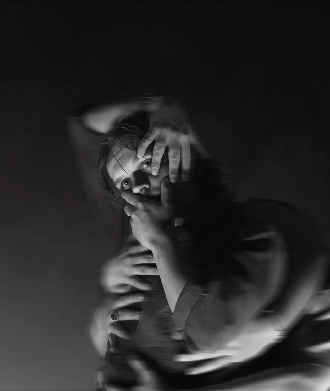 A dramatic black-and-white portrait of a performer with hands covering their face for the play Bull/Fight.