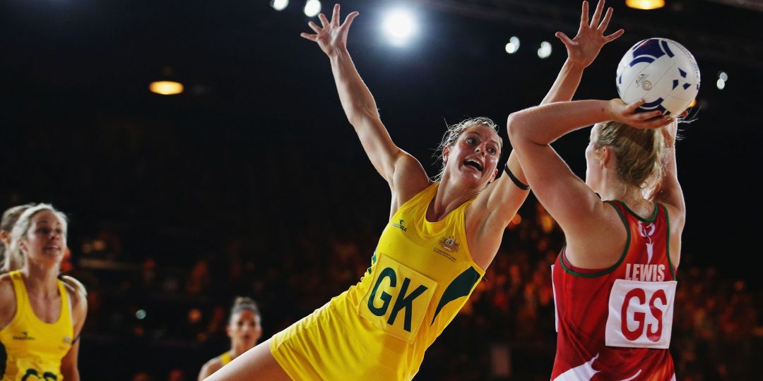 Netball player in a yellow and green kit leaping to intercept the ball at the Commonwealth Games.