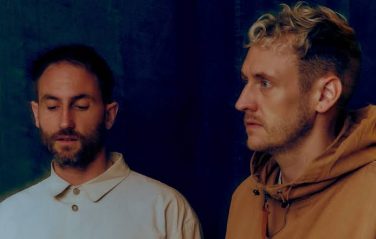 A close-up portrait photograph of the electronic duo Maribou State against a dark, textured blue background, representing one of the top music highlights at the Edinburgh Fringe.