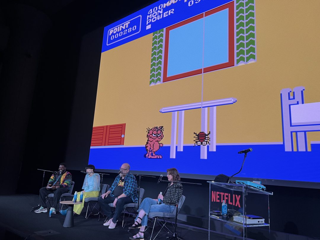 Comedians on stage seated in front of a giant screen projecting a retro video game for Shit Arcade.