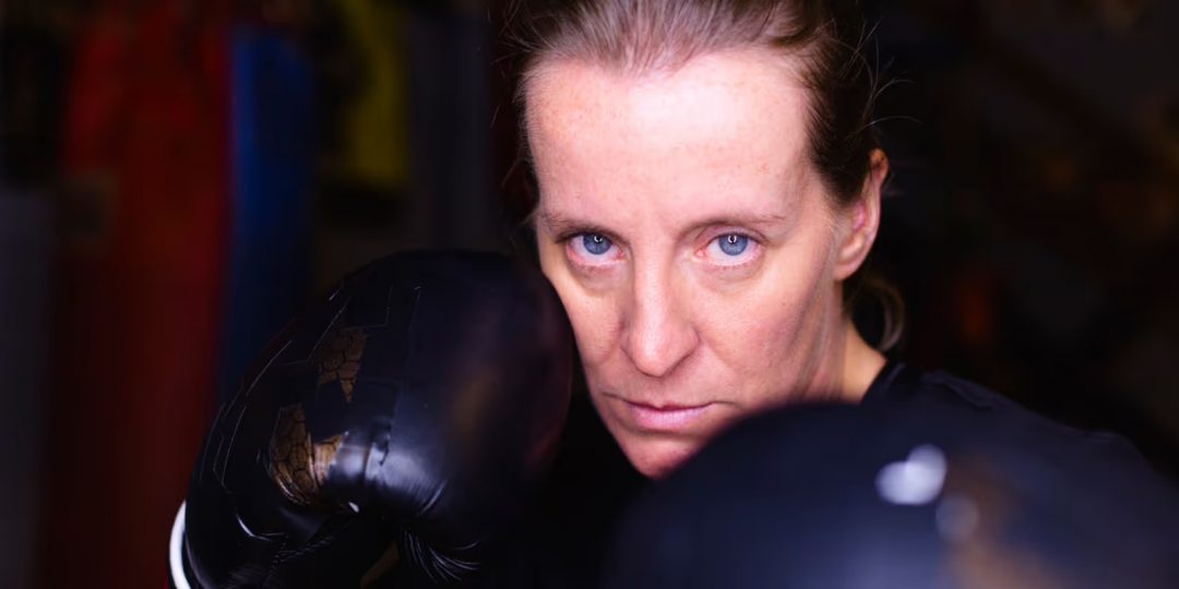 A close-up portrait of a woman wearing black boxing gloves and a focused expression for the Edinburgh Fringe theatre show Slayers.