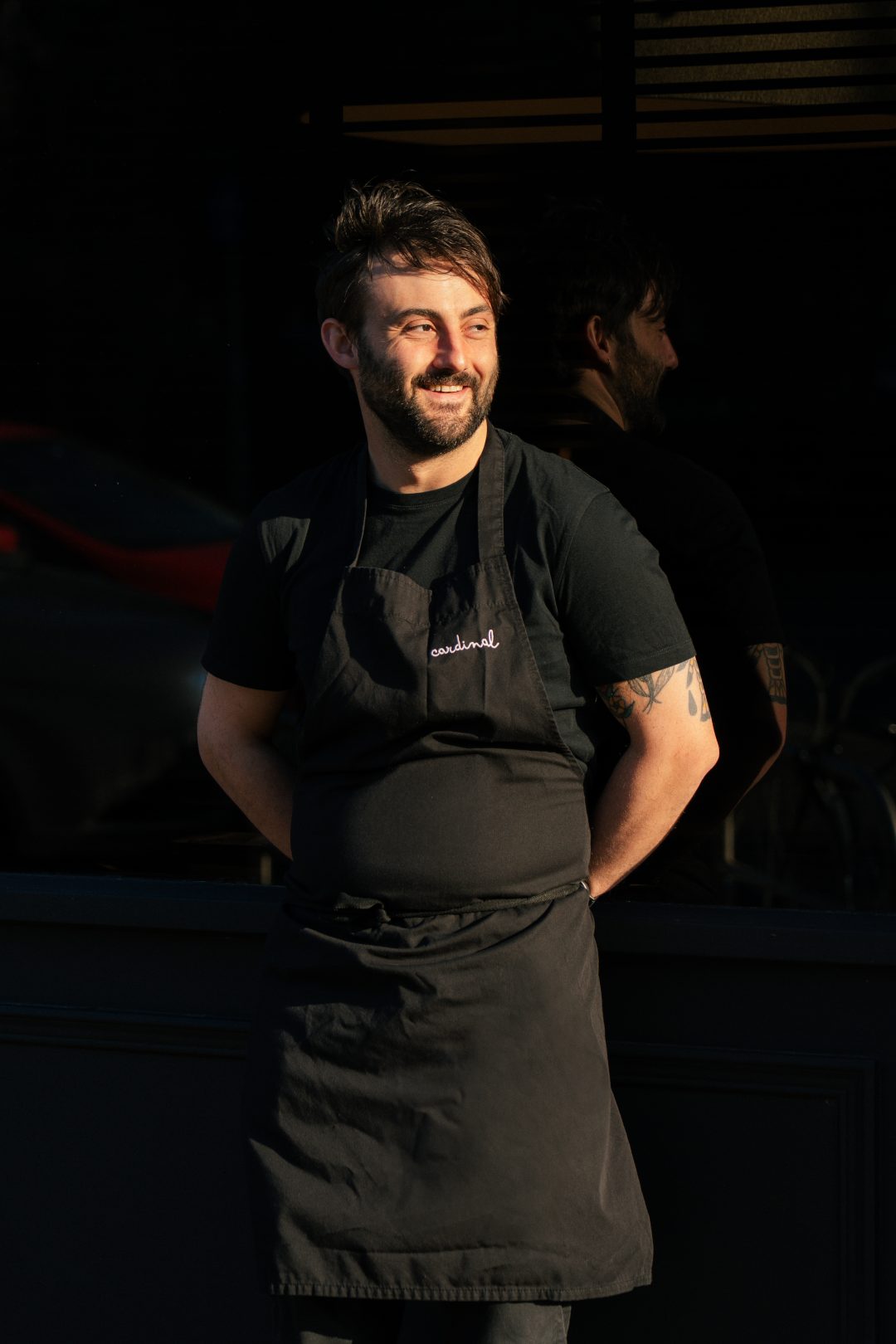Chef Tomás Gormley wearing a black apron standing outside with his hands behind his back.
