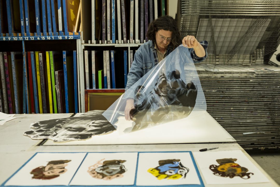 Artist Jamie Fitzpatrick in the print studio working on large-scale screenprints and collaged print pieces on a workbench.