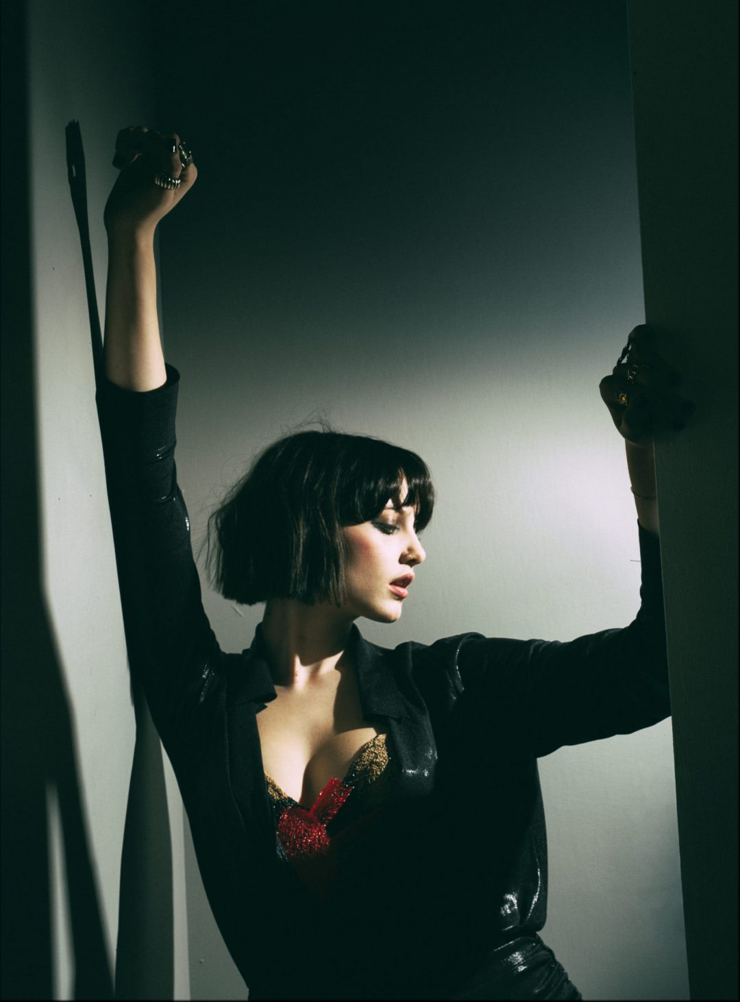 Singer-songwriter Ellijah posing with raised arms against a wall in a black jacket