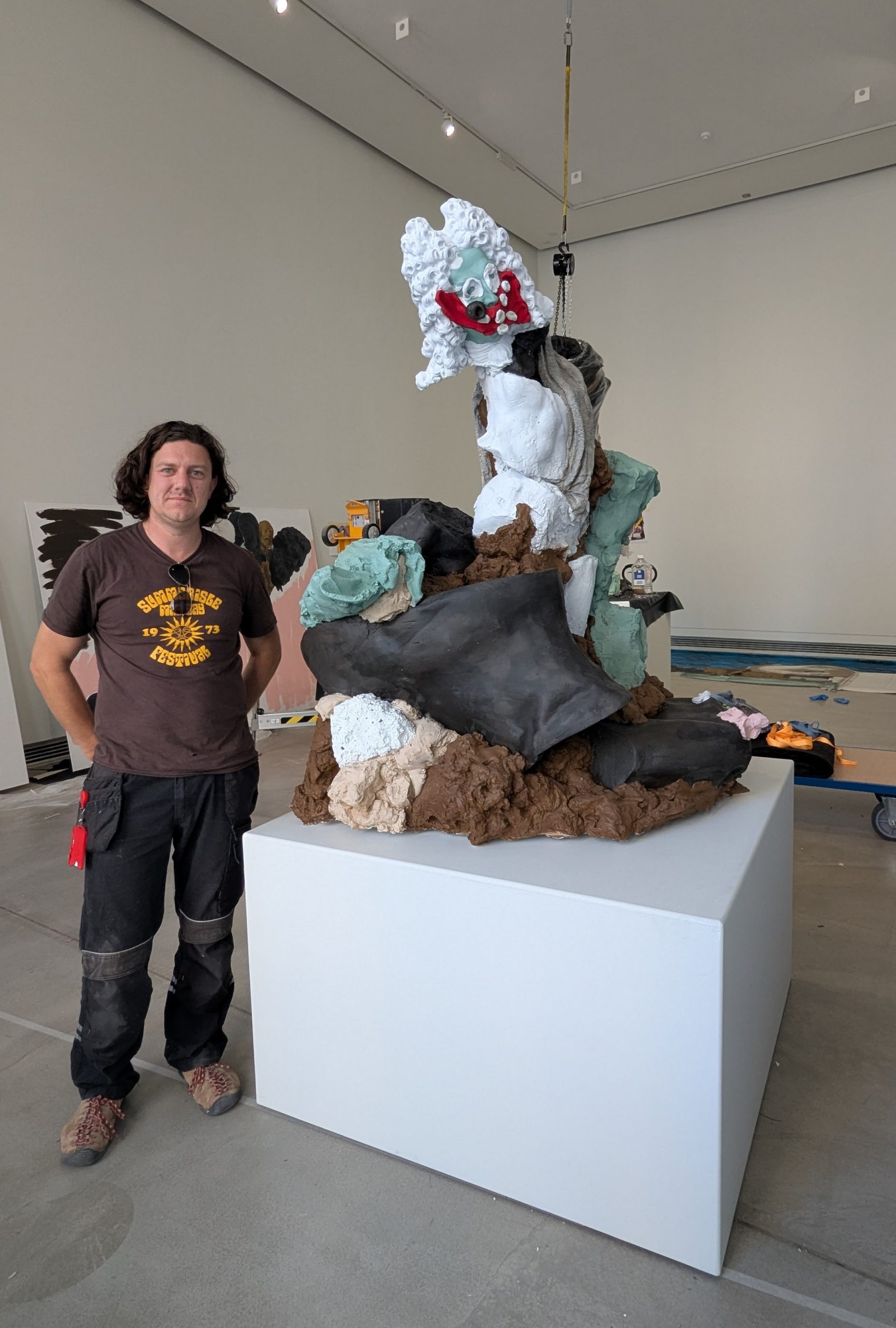 Artist Jamie Fitzpatrick standing next to his sculpture Memorials to Sausage Politics displayed on a white plinth inside the gallery space.