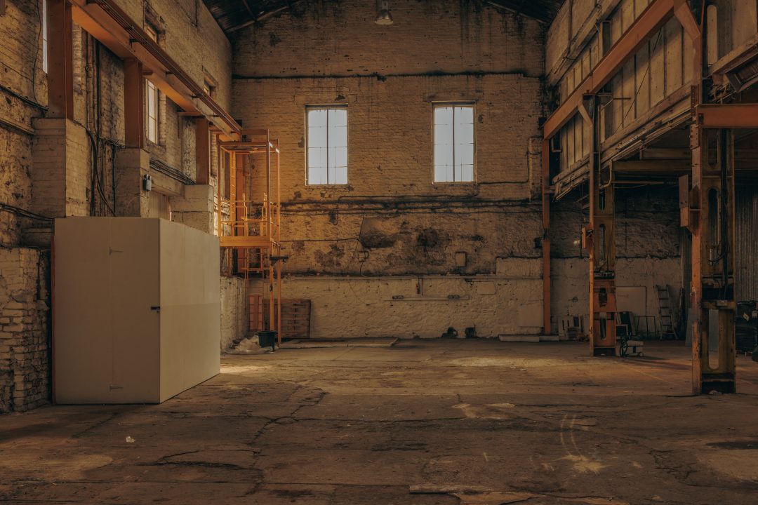 The empty interior of the post-industrial warehouse venue featuring distressed brick walls, iron pillars, and large windows.