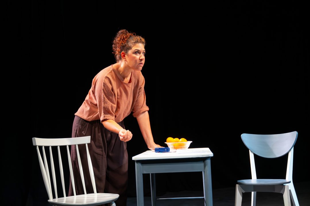 Two actors sitting on the floor side by side holding hands during a performance of For Dolores by Fishamble.