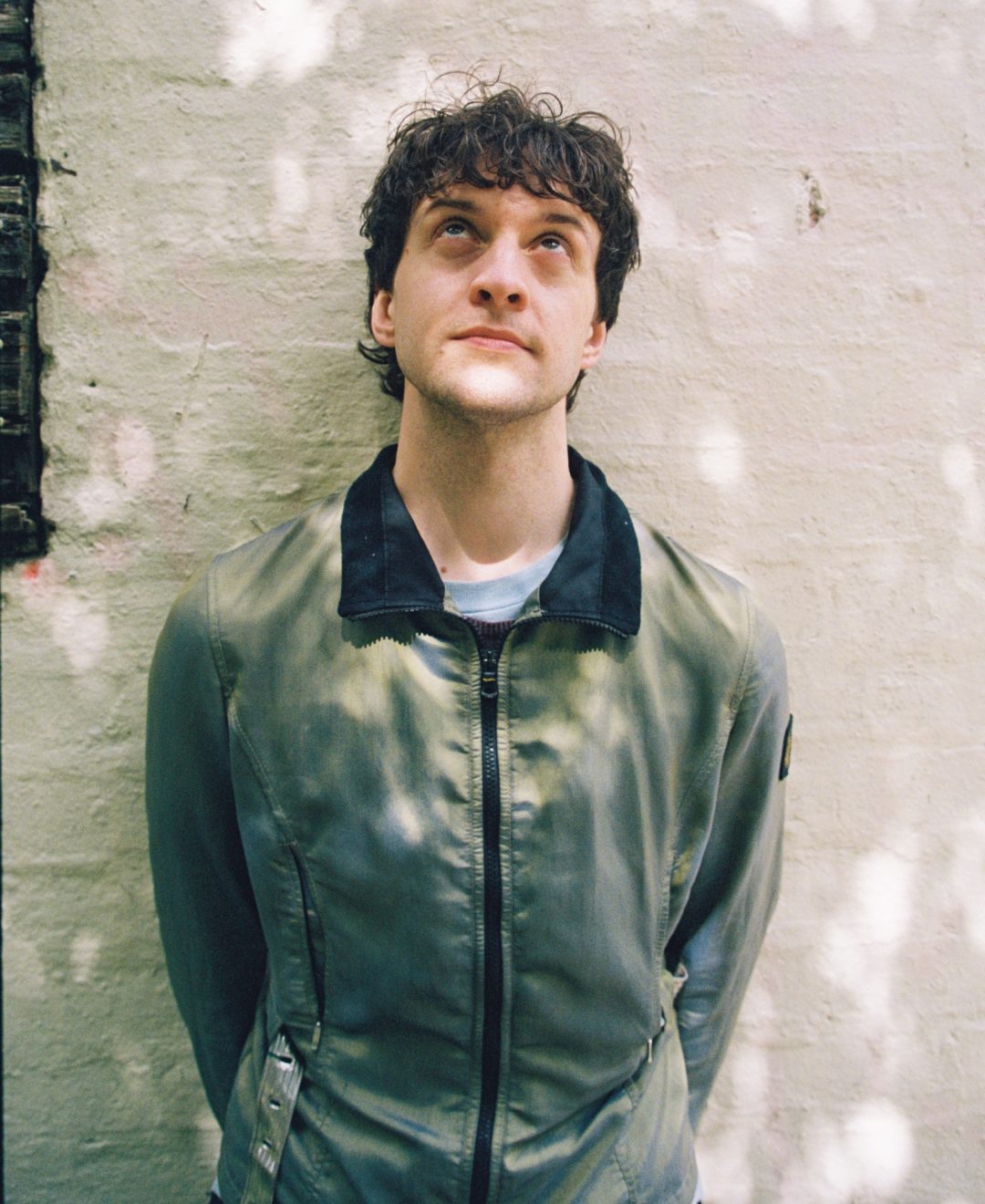 Musician Stanley Welch looking upward while standing against an outdoor wall
