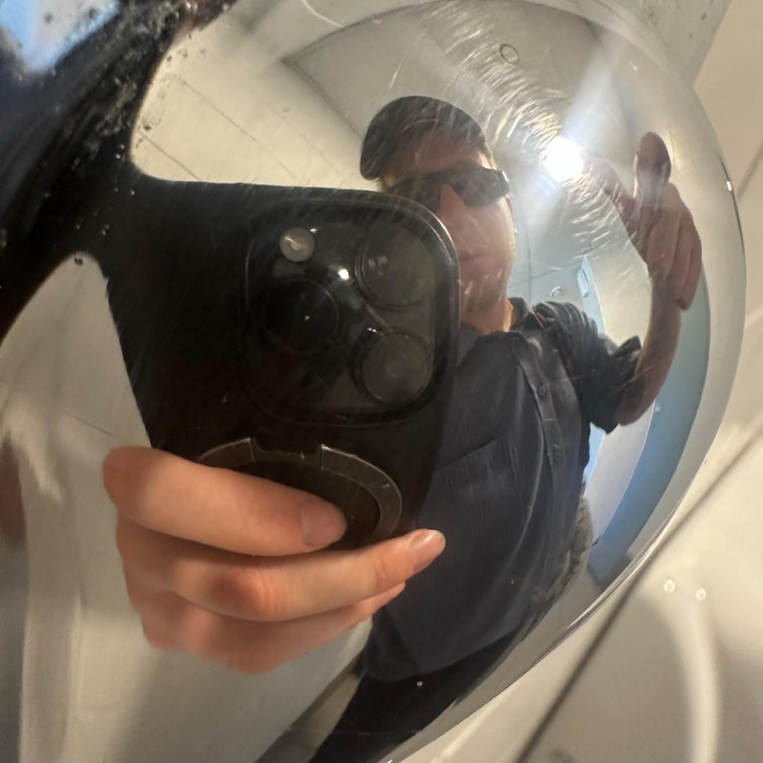 Musician tmrrwkid taking a distorted selfie in a convex mirror wearing sunglasses and a cap