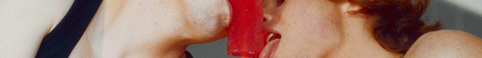 An intimate film still of two young people sharing a red ice lolly, with one wearing a black tank top that reads 'MOMMY NEEDS A CIGARETTE'.