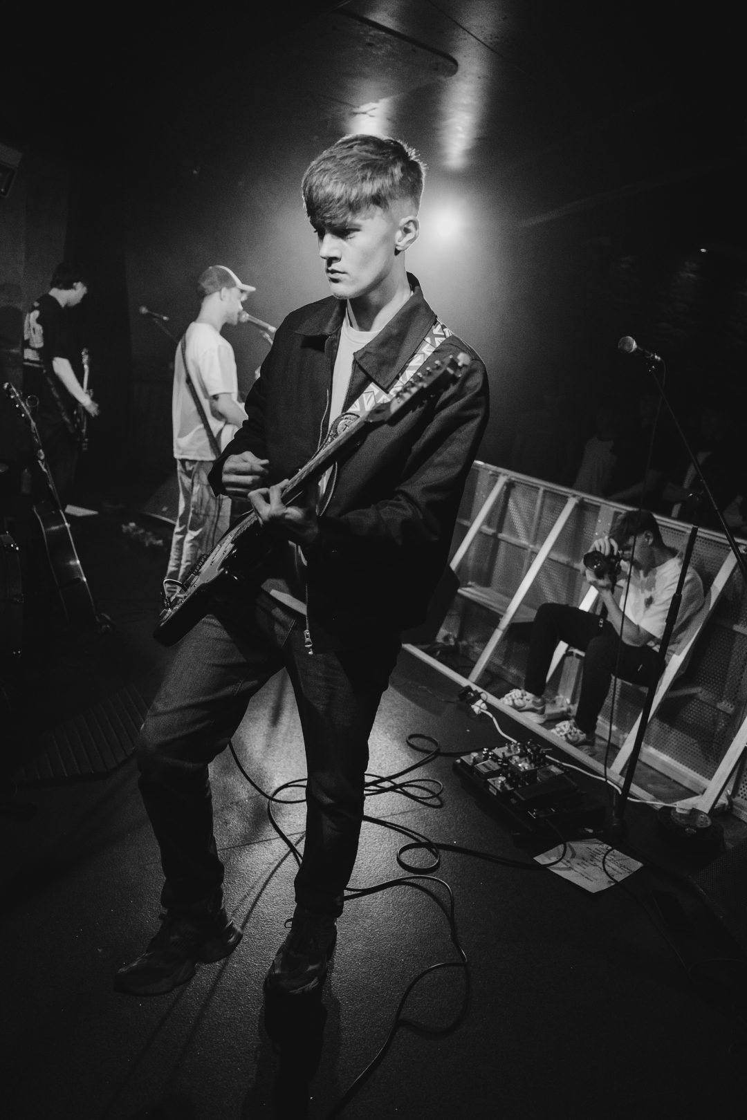 Black and white shot of Blanc guitarist playing an electric guitar live on stage.