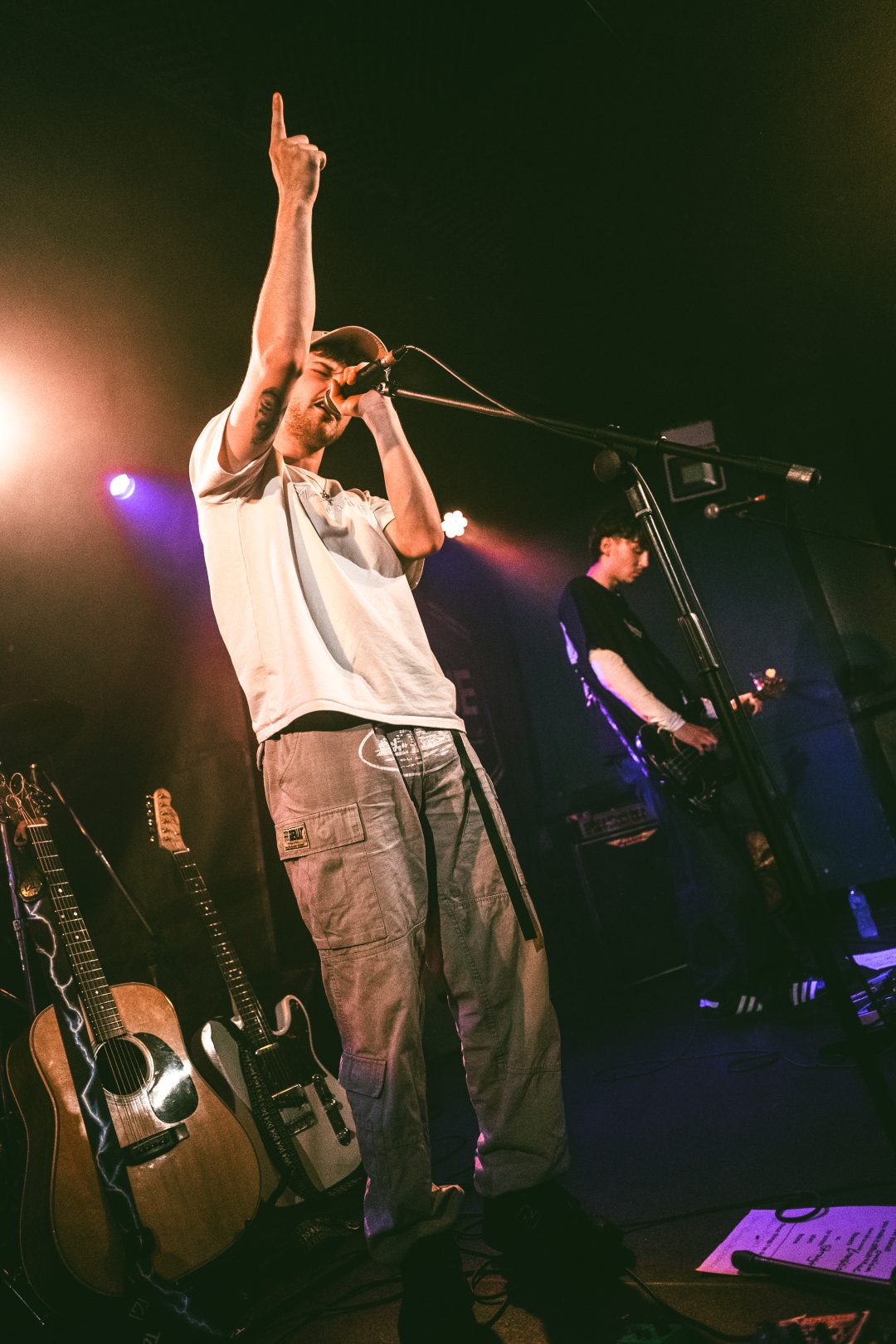 Blanc vocalist singing into a microphone with one arm raised during a live gig on stage.