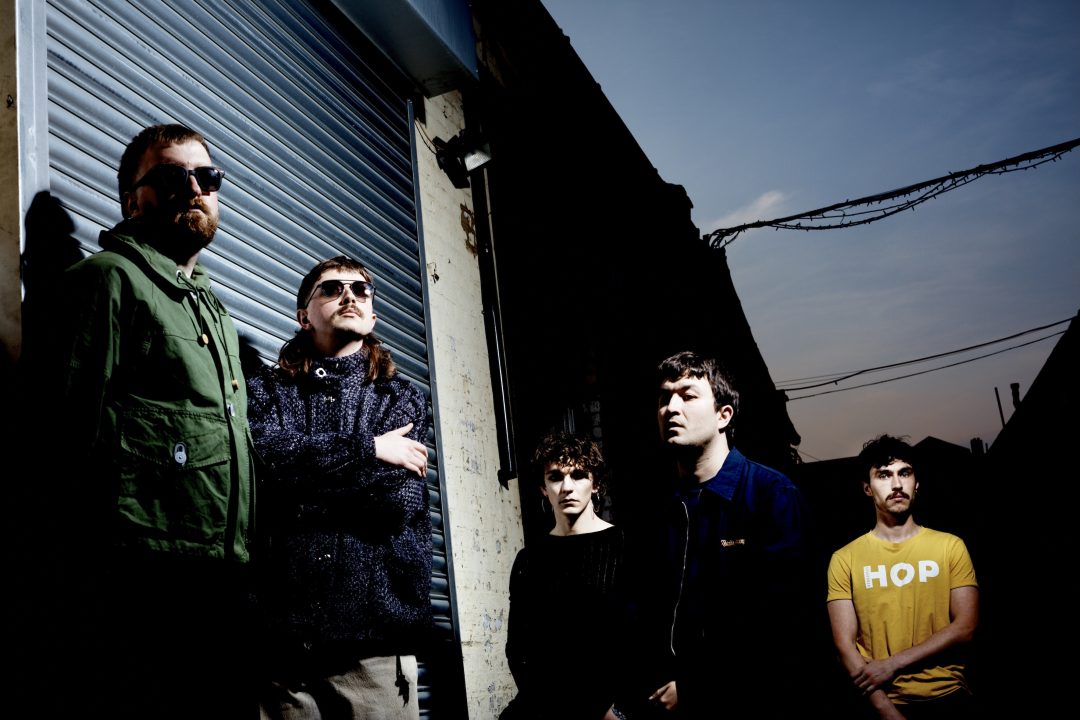 Promotional photo of Irish post-punk band Gurriers in an urban alleyway at dusk, standing dramatically in front of a closed metal roller shutter.