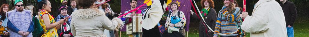 Costumed performers dance with ribbons on a grassy lawn during the Sett Studios Foik Ferly procession.