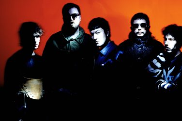 Intense, high-contrast portrait of Gurriers against a vibrant orange background, with shadowy, dramatic lighting creating a moody aesthetic.