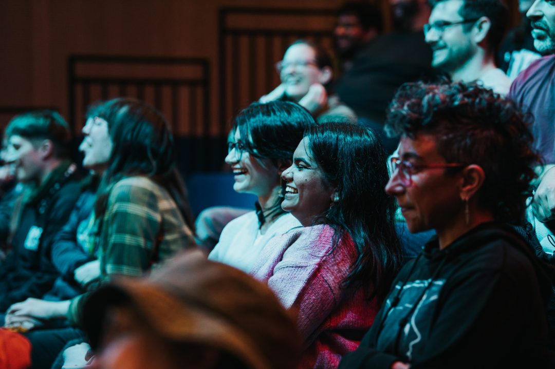 Audience members laughing and smiling during a film screening, seen in a candid side view inside a cinema.